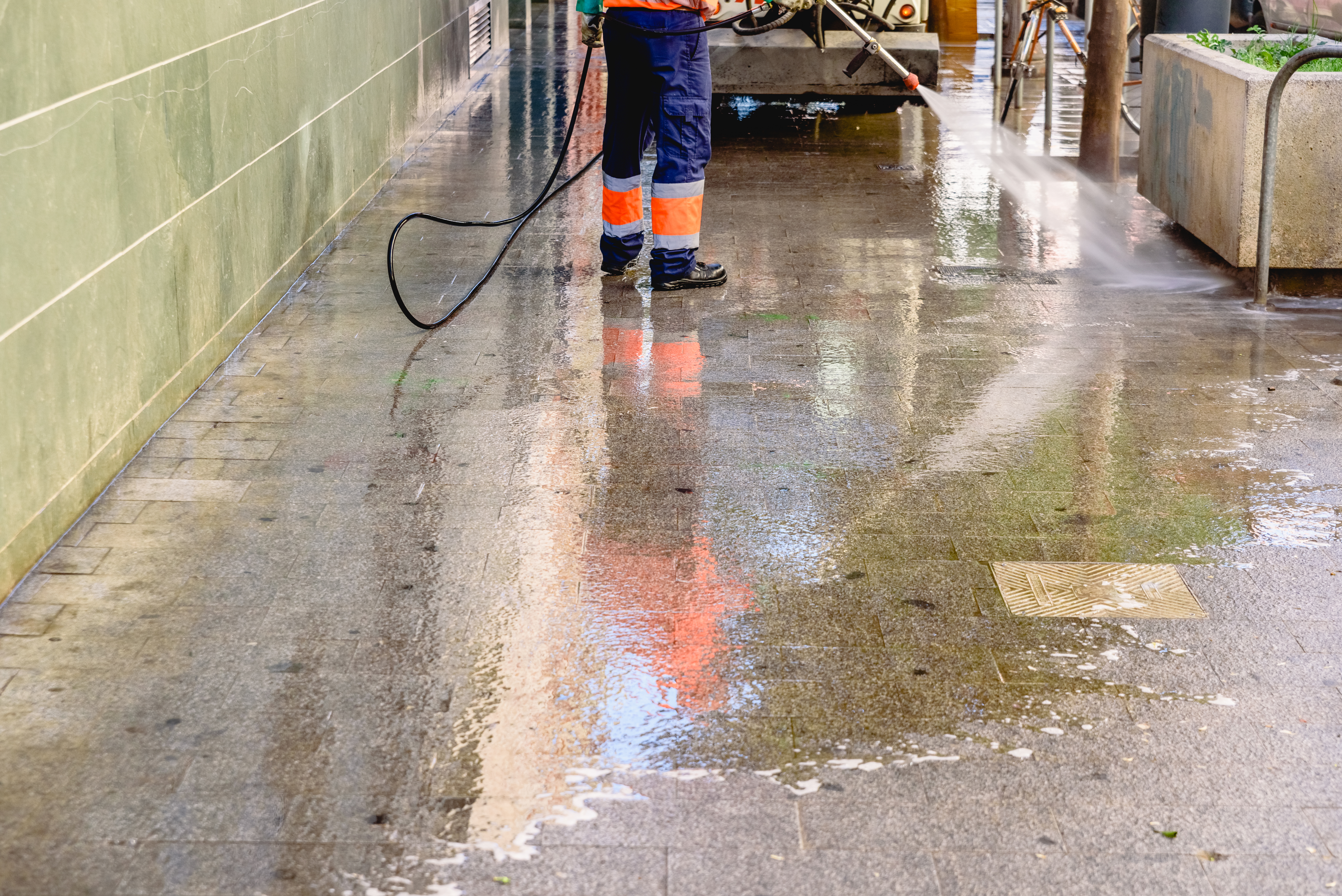 Worker pressure washing pavement surface