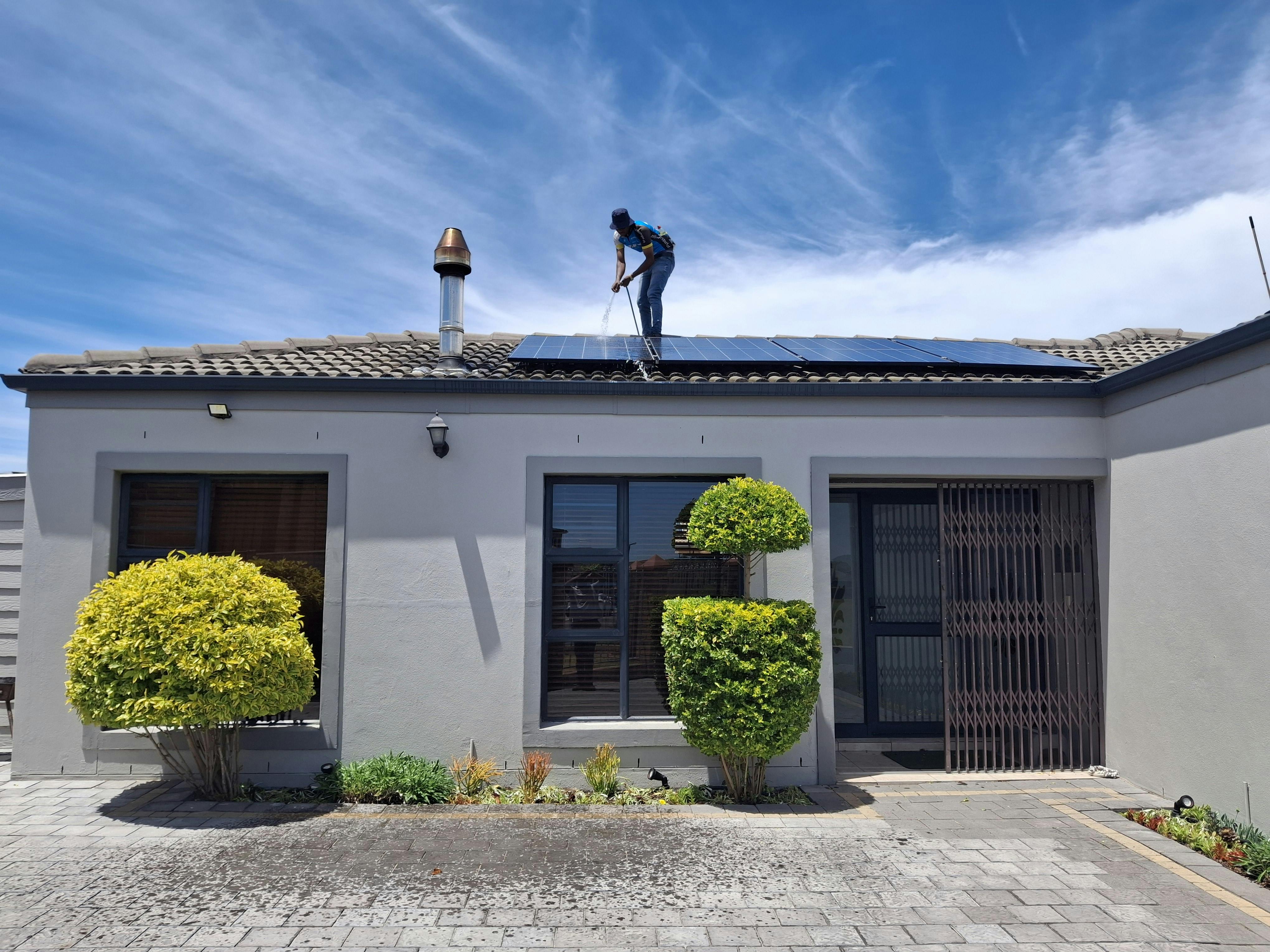 Technician pressure washing solar panels on residential roof